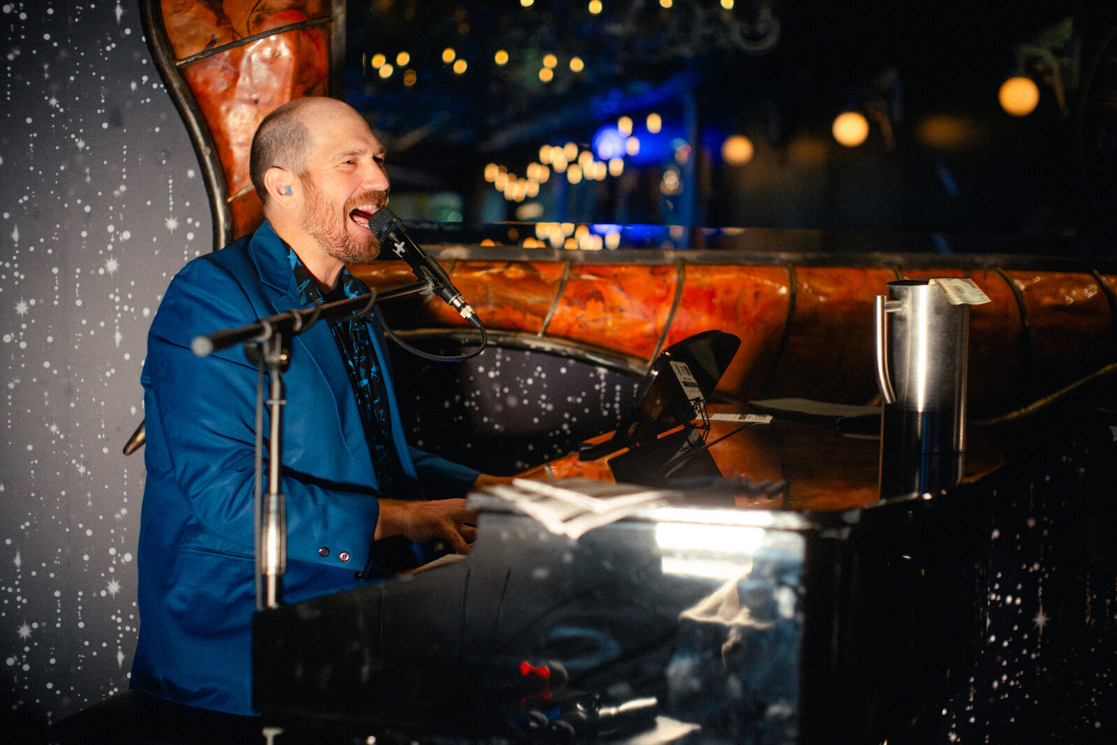 Performer singing at the piano with string lights glowing behind the stage
