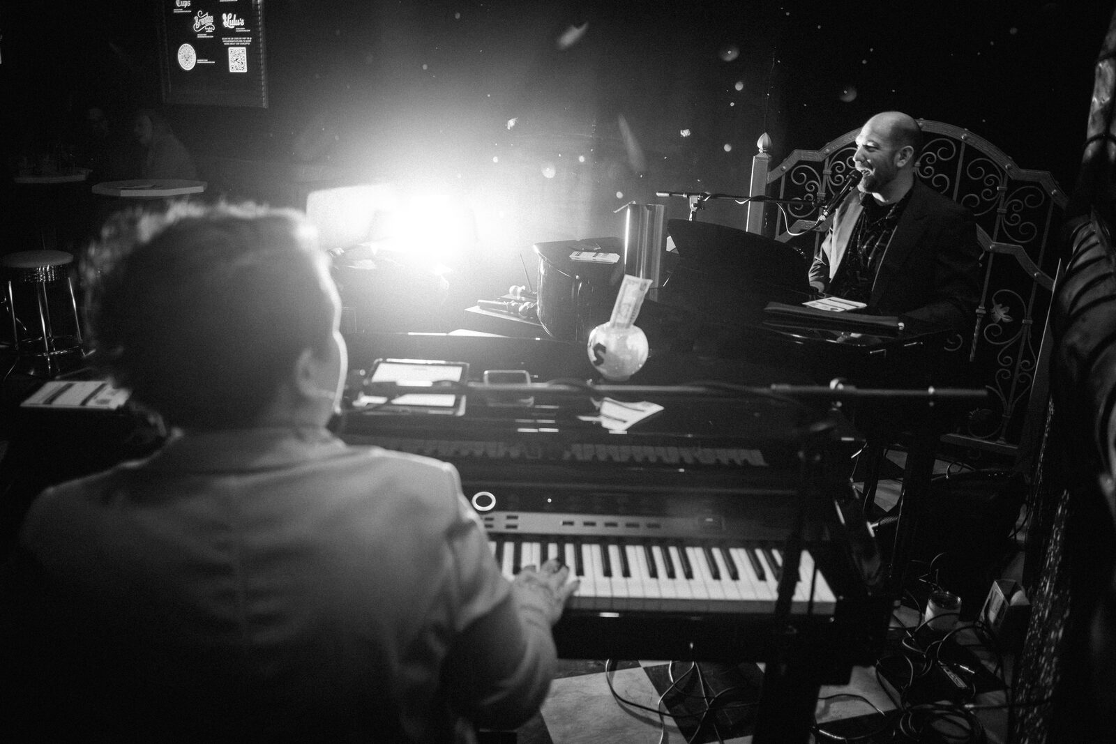 Black and white shot of two performers playing piano and singing together